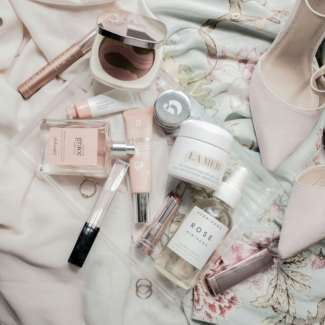 Assorted skincare products and makeup on a clear tray with beige heels