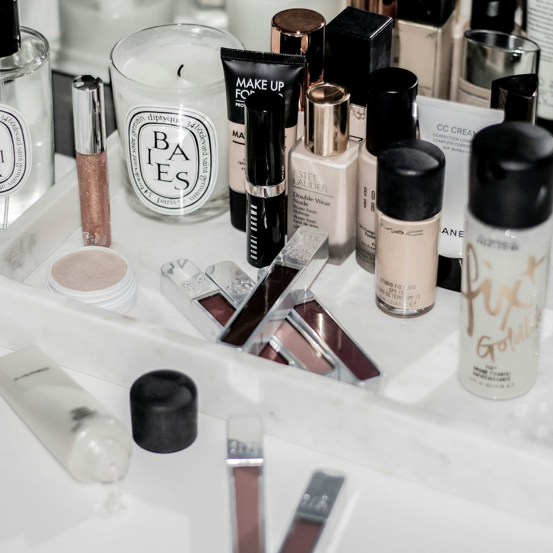 Assorted makeup bottles, tubes, and a scented candle on a white marble tray